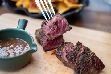 Medium rare meat on fork with wooden plate on the background