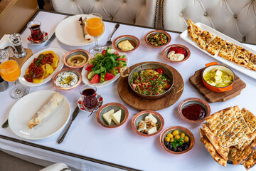 Turkish breakfast table. Flat-lay of peoples hands taking pastries, vegetables, greens, olives,...