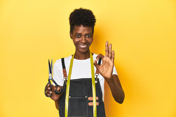African tailor with scissors and measuring tape, fashion concept cheerful and confident showing ok gesture.