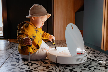 Baby on the floor with robot vacuum cleaner. Child repairs and play with robot vacuum cleaner. Home...