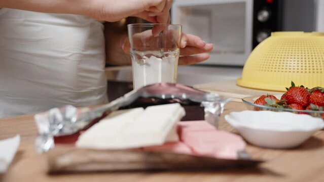 The woman stirs the melted white chocolate while strawberries and chocolate bars are laid out next to each other on the table.