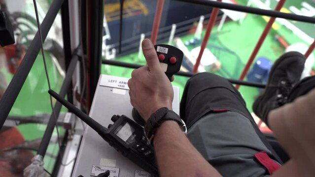 Crane operator works. Hand pulls joystick toward. Inside crane cabin.