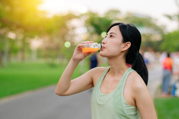 Female jogger. Fit young Asian woman with green sportswear drinking organic orange juice after running and enjoying a healthy outdoor. Fitness runner girl in public park. Wellness being concept