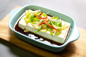 Vegan silken tofu is served hot or cold with a savory soy sauce flavored with sesame oil, ginger and green onions .