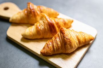 Fresh croissant on wooden board with nature sunlight through window.