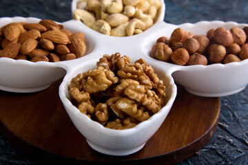 Assorted hazelnuts, cashews, almonds and walnuts on a white platter on a wooden stand. A variety of healthy nuts for snacking and healthy nutrition