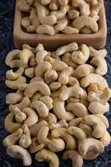 Close-up of dried cashew nuts placed arbitrarily on a textured gray background. Delicious cashew nuts on the table and in a wooden bowl