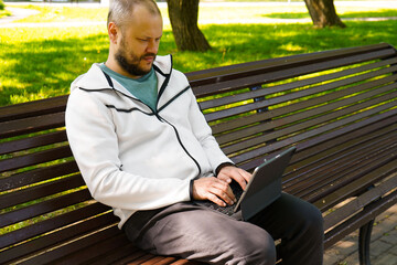 Fototapeta premium Man freelancer holding black tablet pc with mock up green desktop screen sitting on a bench in the park