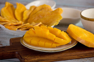 The juicy flesh of a ripe yellow mango is sliced on a plate and the candied fruit slices are laid out on a saucer. Close-up of tropical delicious ripe mango fruit on a beautiful dish