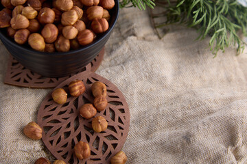 Plate of hazelnuts stands on a figured wooden stand in the shape of a leaf on burlap. Delicious nut, nutritious hazelnuts in a black cup on old burlap and a coniferous branch