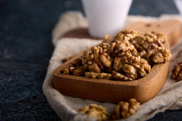 On a black table, old burlap, halves of peeled walnuts are laid out in a wooden plate. Peeled, dried walnut halves used as a snack or for baking