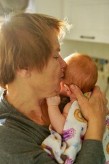 an elderly woman, a grandmother, in the rays of the morning sun, hugs and kisses her grandson, a newborn baby
