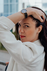 
beautiful young woman in a white jacket and black trousers with an open belly and a tattoo in the city against the backdrop of glass buildings