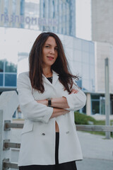 
beautiful young woman in a white jacket and black trousers with an open belly and a tattoo in the city against the backdrop of glass buildings