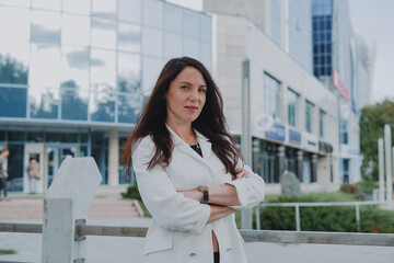 
beautiful young woman in a white jacket and black trousers with an open belly and a tattoo in the city against the backdrop of glass buildings