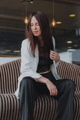 
beautiful young woman in a white jacket and black trousers with an open belly and a tattoo in the city against the backdrop of glass buildings