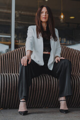 
beautiful young woman in a white jacket and black trousers with an open belly and a tattoo in the city against the backdrop of glass buildings