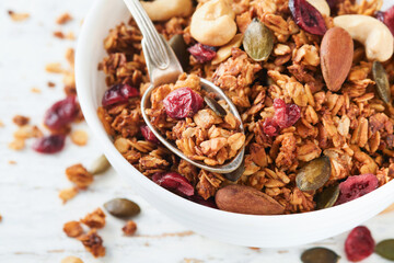 Homemade granola in glass jar with greek yogurt or milk and cashews, almonds, pumpkin with dried cranberry seeds in on white rustic wooden table background. Healthy energy breakfast or snack. Top view