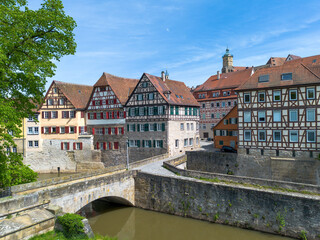 Obraz premium Schwaebisch Hall, half-timbered old town houses with a view of the church tower, the Kocher river with an old arched bridge, drone shot