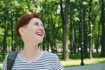Portrait of a middle-aged woman with short red hair in a striped t-shirt. Woman looks away and laughs. Walk in the city park.