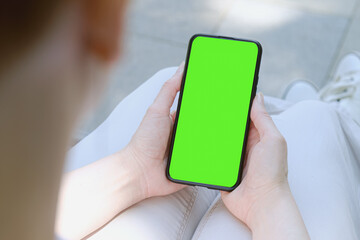 Woman is holding a smartphone in front of her. Green screen, copy space and chroma key on smartphone screen. Template for inserting an image on device screen.
