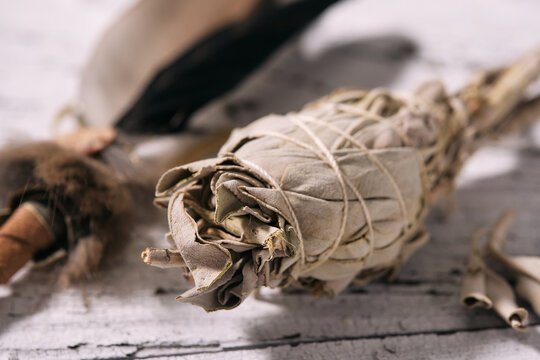 Close up of a smudge stick with White Sage (Salvia apiana) and incense feather on old white wood
