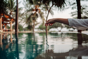 The graceful touch of a woman's hand on the turquoise water surface creates ripples, symbolizing...