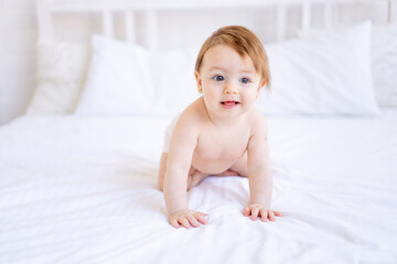 a joyful baby girl of six months on a bed in a diaper crawls and smiles, a small child on a cotton...