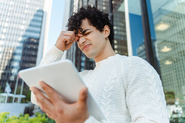 Portrait of sad latin businessman holding digital tablet working outdoors, headache, failed business