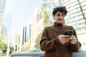 Fototapeta na wymiar Portrait of handsome latin man holding mobile phone checking email standing on urban city street