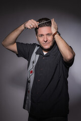 Vertical studio portrait of a 40 years old man in rockabilly style combing his hair with a steel...