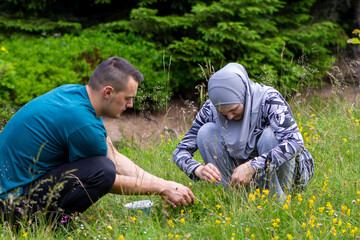 Young muslim couple picking blueberries in the forest. Boy and girl collecting organic wild bilberries, lifestyle and agricultural concept