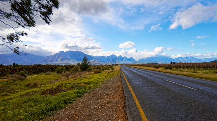 A beautiful view over a wet road towards majestic cloud covered mountains near Worcester, Western Cape, South Africa.
