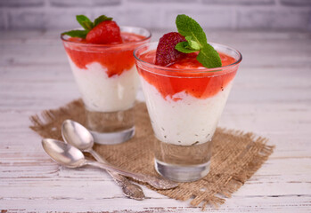 Rice pudding with strawberry jam in glasses on a wooden background.
