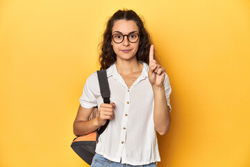 Caucasian university student with glasses, backpack, showing number one with finger.