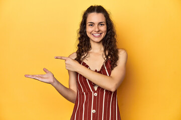 Young Caucasian woman, yellow studio background, excited holding a copy space on palm.