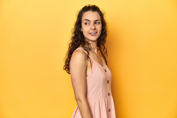 Young Caucasian woman, yellow studio background, looks aside smiling, cheerful and pleasant.