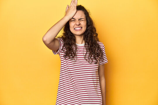 Young Caucasian woman, yellow studio background, forgetting something, slapping forehead with palm and closing eyes.