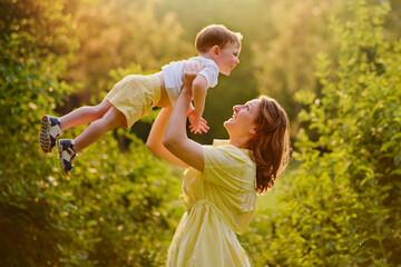 A mother woman plays with a child in nature, lifting and tossing him in her arms. Toddler baby and...