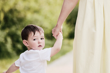 Child boy looks back with fear in his eyes, clutching his mother's hand tightly. Little baby feels...