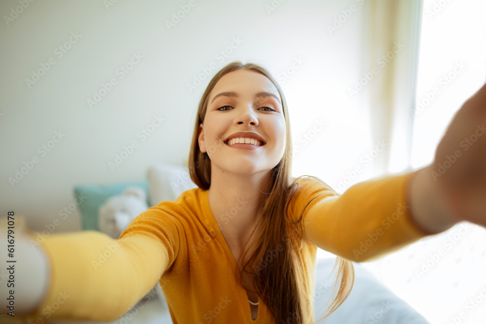 Wall mural Cheerful Blonde Young Lady Making Selfie Sitting In Modern Bedroom