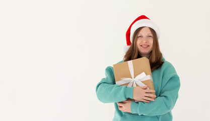 Pretty overjoyed lady holding large giftbox close to chest wear green hoodie and santa hat isolated white background