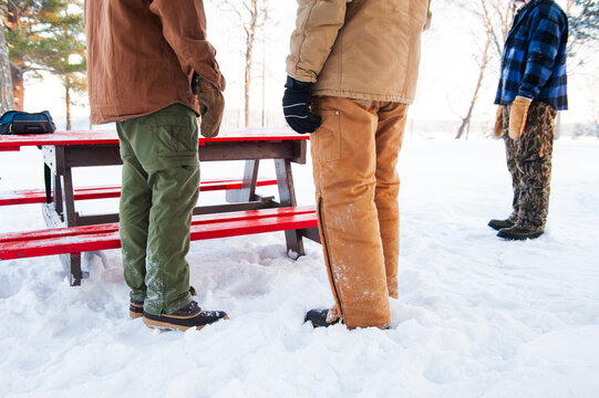 Three men wearing winter clothes and mittens stand next to a picnic bench in Minnesota in the winter.