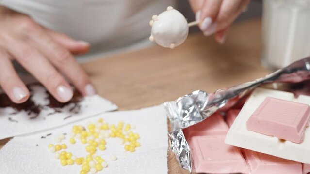The woman is decorating the white chocolate-covered strawberries with colorful sugar pearls.