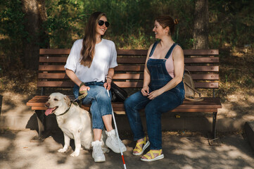 Blind caucasian woman sitting on bench with guide dog and pregnant friend. 