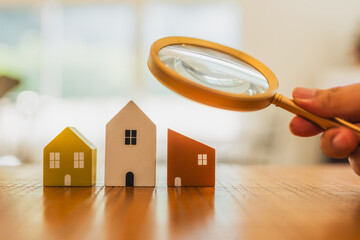 Hand holding magnifying glass and looking at house model, house selection, real estate concept.