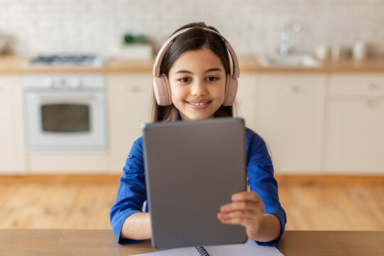 Cheerful school girl holding digital tablet wearing headphones at home