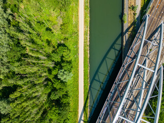 Aerial view of metal railway bridge over the water of a river, with the forest and field aside it....