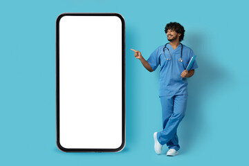 Happy indian doctor surgeon pointing at huge smartphone, mockup