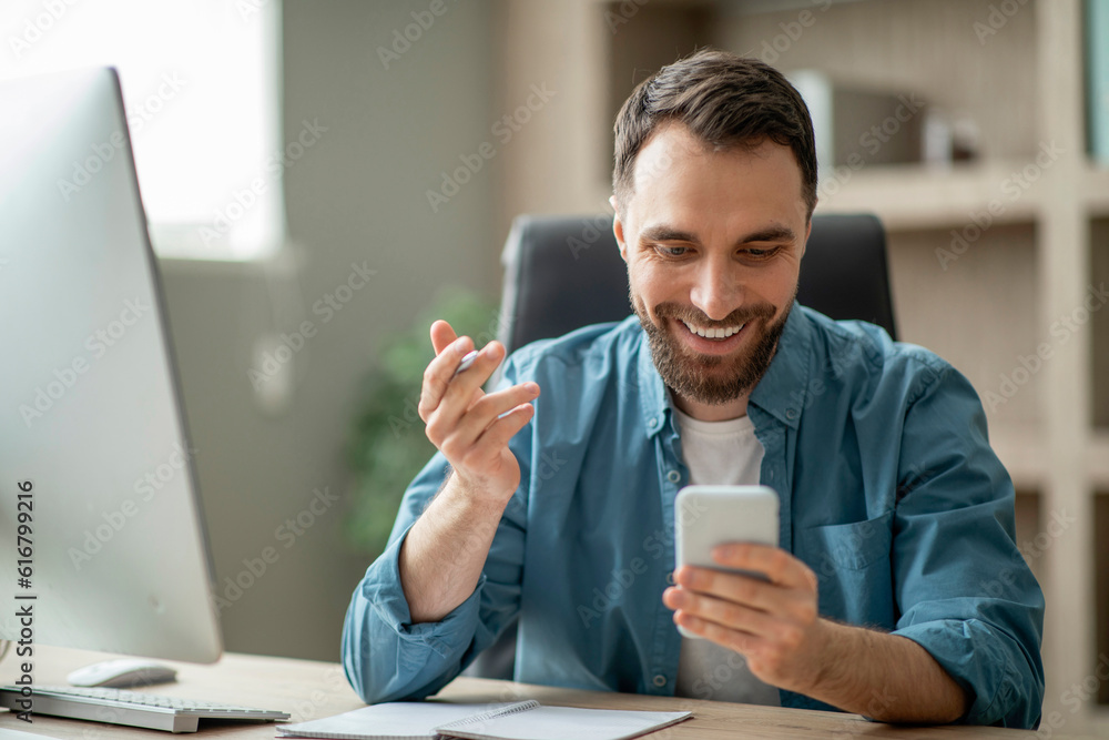 Poster smiling handsome young businessman checking business mobile app while working at office